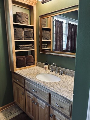 A bathroom with a wooden vanity, a sink, and a mirror. - Whispering Oaks Cabin 13 (Oden)