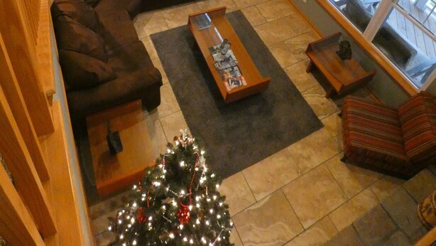 Amplia sala de estar con un sofá modular grande, una mesa de centro y un árbol de Navidad. Se ve una cocina al fondo, con una mesa de comedor y sillas.