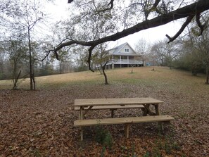 A picnic table in a wooded area with a house in the background. - Whispering Oaks Cabin 13 (Oden)