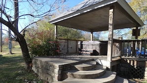 Un espacio al aire libre techado con un jacuzzi, una escalera de piedra y una mesa y sillas de metal.