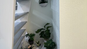Eine Treppe mit weißer Geländer, umgeben von Kübelpflanzen und einem kleinen Steingarten am Fuß.