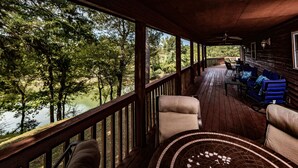Une terrasse en bois avec des sièges extérieurs et une vue sur un lac entouré d’arbres.