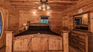 Une chambre dans une cabane en bois, avec un lit, une commode et un ventilateur de plafond.