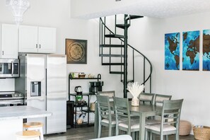 A modern kitchen with white cabinets, a stainless steel refrigerator, a microwave, and a coffee maker. There is a dining table with four chairs and a spiral staircase leading to an upper level. - Peaceful Lakefront Getaway with Ping Pong on Apple Valley Lake (Howard)
