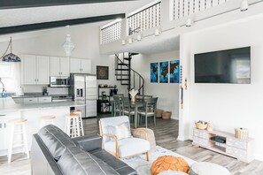 A spacious living area with a modern kitchen, a dining set, and a staircase leading to an upper level. - Peaceful Lakefront Getaway with Ping Pong on Apple Valley Lake (Howard)
