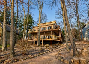 A multi-story wooden cabin with a deck, surrounded by trees and a dirt path. - Peaceful Lakefront Getaway with Ping Pong on Apple Valley Lake (Howard)