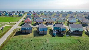 An aerial view of a residential area with houses of various colors, a main road, and a clear view of the ocean in the background.