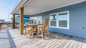 A covered outdoor deck with a wooden table and chairs, a railing, and a view of the ocean.