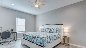 A bedroom with a bed, desk, chair, and a standing lamp.