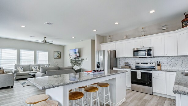 A modern kitchen with white cabinets, a granite countertop, and a built-in oven. There are three wooden stools at the island.