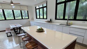 A modern kitchen with a large island, bar stools, and large windows offering a view of greenery. - Modern Beach Home with Pool & Rooftop - 150 metros (Santa Cruz, Playa Avellanas)