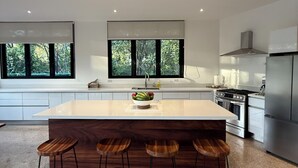 A modern kitchen with a large island, bar stools, and a view of greenery through the windows. - Modern Beach Home with Pool & Rooftop - 150 metros (Santa Cruz, Playa Avellanas)