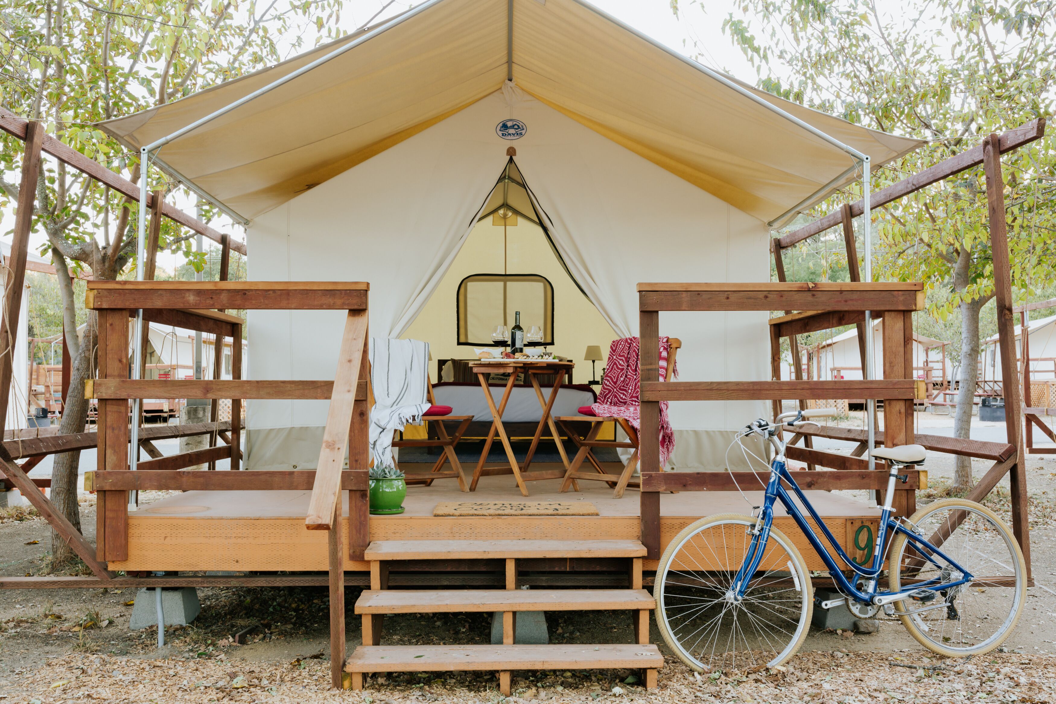 Una carpa con una mesa y sillas al frente, una bicicleta y un pequeño jardín.