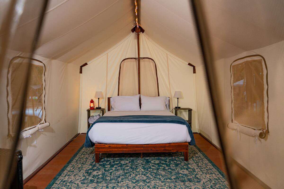 Een tent met een bed, twee nachtkastjes en een kamerkleed met patroon.