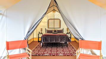 A tented room with a bed, two wooden chairs, and a patterned rug.
