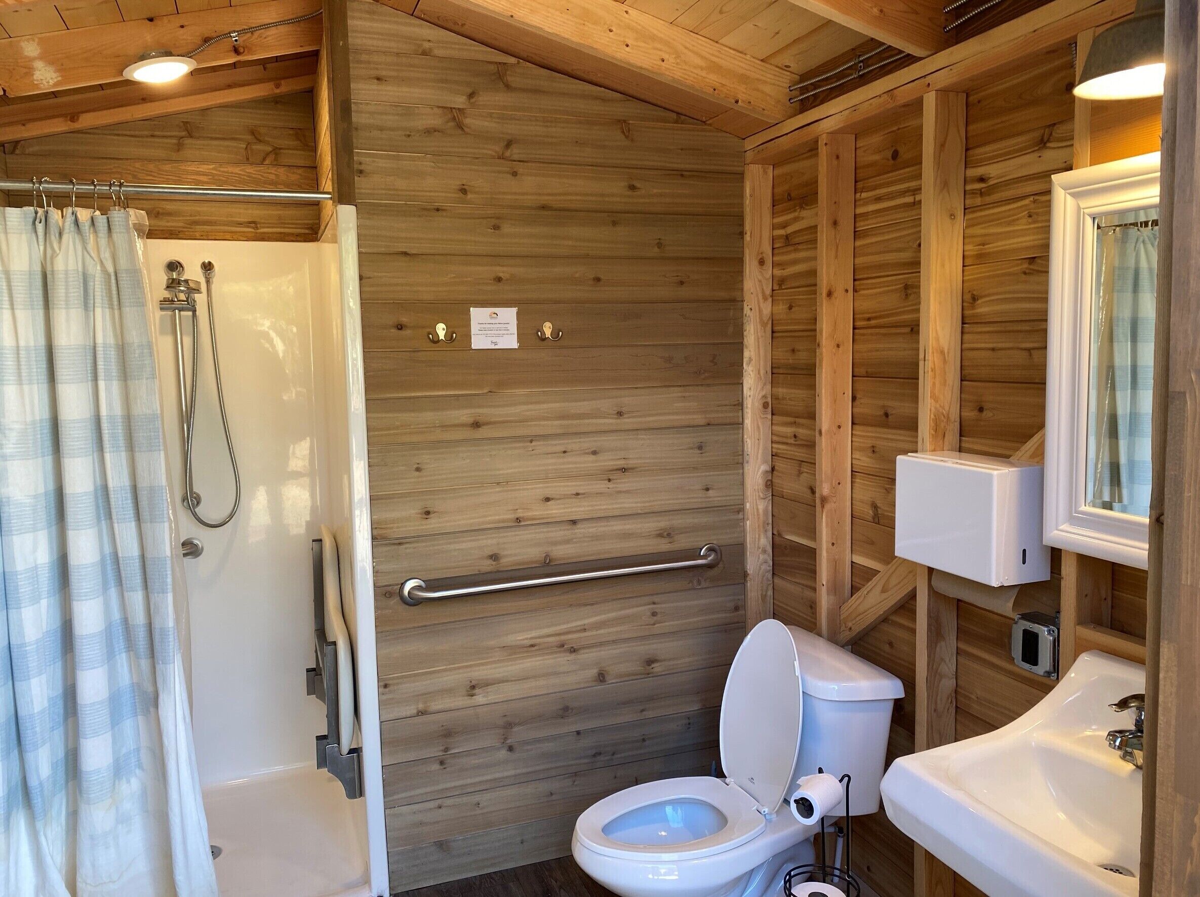 A wooden cabin bathroom with a shower, toilet, and sink.