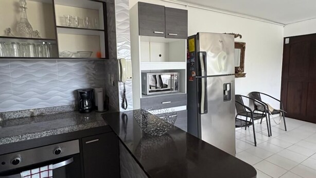 A modern kitchen with a marble countertop, built-in appliances, and a dining area with chairs. - VISTA AL MAR (Santa Marta)