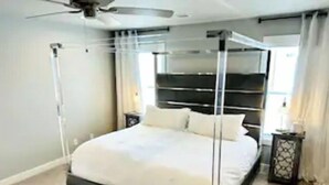 A four-poster canopy bed with a black frame and white bedding, a bedside table with a lamp, and a window with curtains. - Newburgh Newsie - 3BR, 2.5BA, Gym, Patio, New Construction in Amazing Location! (Newburgh)