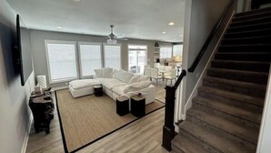 A spacious living room with a large sectional sofa, a wooden staircase, and a view of the kitchen. - Newburgh Newsie - 3BR, 2.5BA, Gym, Patio, New Construction in Amazing Location! (Newburgh)