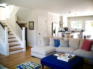 Relax in a spacious living area with a large L-shaped sofa and matching ottoman, complemented by a staircase leading to an upper level and a modern kitchen.
