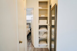 A walk-in closet with shelves and drawers, containing neatly folded towels and pillows.