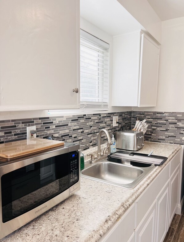 A compact kitchen with a built-in microwave, stainless steel sink, and a window with blinds.