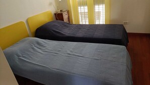 Une chambre avec deux lits simples, une table de chevet en bois avec une radio et une fenêtre avec des rideaux jaunes.