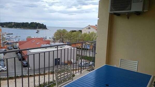 Un balcon doté d’un sol bleu, d’une chaise blanche et offrant une vue sur une marina avec des bateaux et une île lointaine.