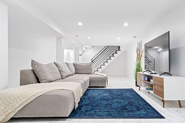 A modern living room with a sofa, a blue rug, a TV, and a staircase.