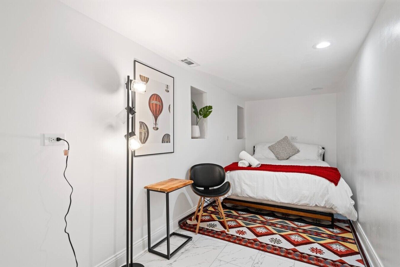 Een slaapkamer met een bed, een stoel, een vloerlamp en een plant aan de muur.