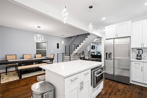 Una cocina moderna con armarios blancos, una isla de mármol, electrodomésticos de acero inoxidable y una zona de comedor con banco.