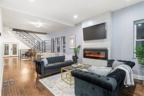 A modern living room with a fireplace, a staircase, and a large TV.