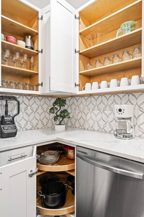 A kitchen with open cabinets, a coffee maker, a blender, and a potted plant.