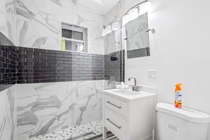 A bathroom with a white vanity, a shower, and a tiled wall with a black and white pattern. - Stunning & Spacious 7BD Home with garage! (Chicago)