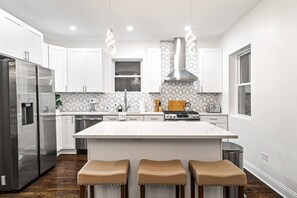A modern kitchen with white cabinetry, a central island, stainless steel appliances, and a patterned backsplash.