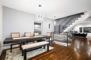A modern dining area with a dark wooden table, beige chairs, a bench, and a chandelier.
