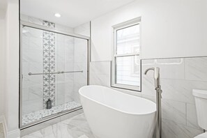 A modern bathroom with a glass-enclosed shower, a freestanding bathtub, and a window providing natural light.