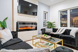 Una sala moderna con chimenea, dos sofás, una mesa de centro y un ventanal grande.