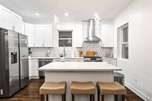 A modern kitchen with white cabinetry, a central island, stainless steel appliances, and a patterned backsplash. - Stunning & Spacious 7BD Home with garage! (Chicago)