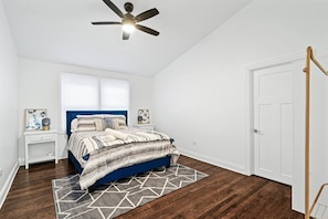 Un dormitorio con cama, mesitas de noche, ventilador de techo y una puerta.