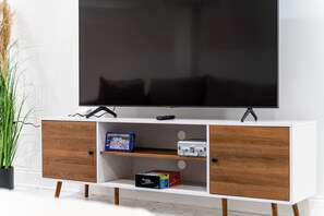 A white TV stand with a flat-screen TV, two wooden cabinets, and shelves holding board games.