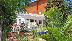 A white building with multiple windows and a covered patio area with potted plants. - Tropical Oasis with Pool  Main Street-3 bedrooms (caye caulker)