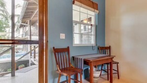 A room with a wooden table and two chairs, a window with a blind, and a view of a balcony. - Tropical Oasis with Pool  Main Street-3 bedrooms (caye caulker)