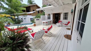 A wooden deck with white chairs and a table, a pool, and a building with a white facade. - Tropical Oasis with Pool  Main Street-3 bedrooms (caye caulker)