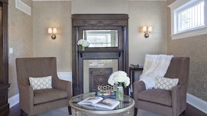 A room with two armchairs, a glass coffee table, a fireplace, and decorative wall sconces. - Edwards House (Fort Collins)