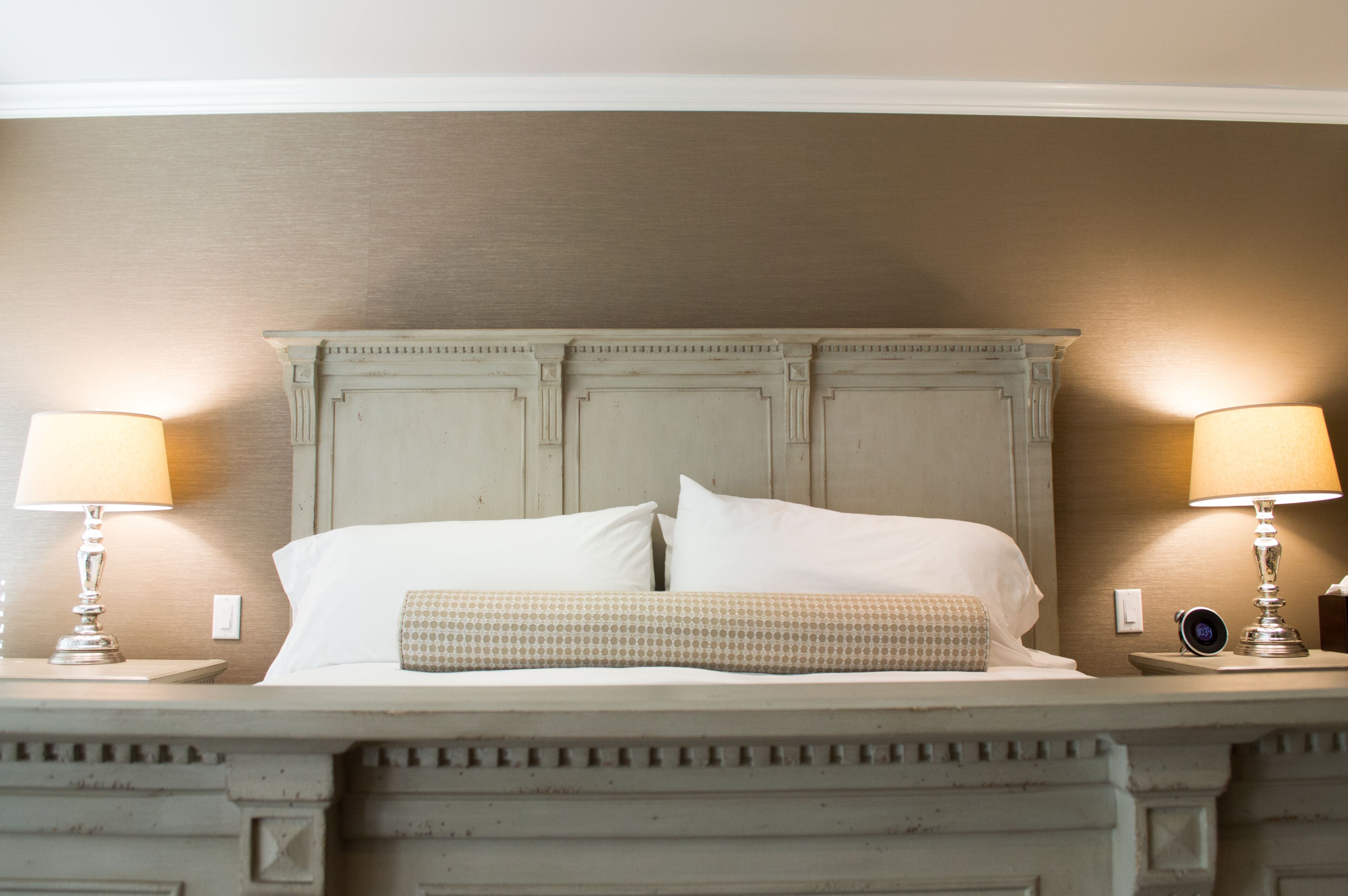 A neatly made bed with white linens and a patterned pillow, flanked by two bedside lamps on a wooden nightstand.