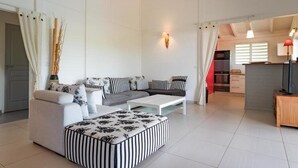 A modern living room with a sofa set, a striped ottoman, and a coffee table. There is a kitchen area visible in the background.