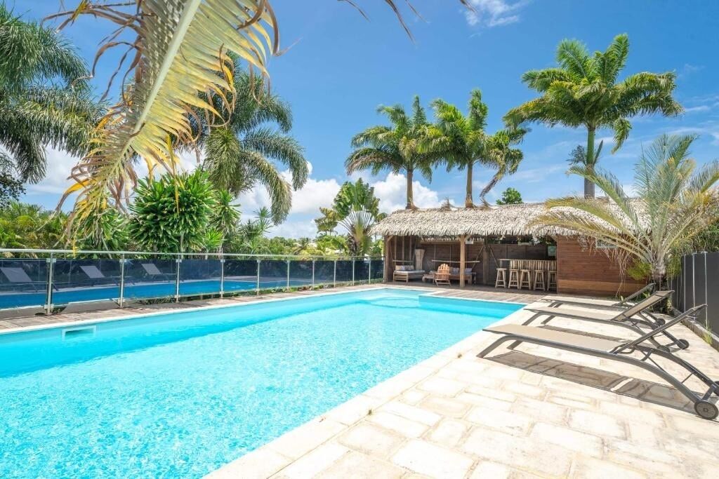 A swimming pool with lounge chairs and a thatched-roof structure.