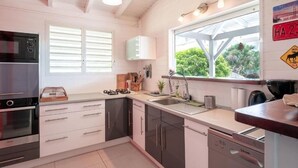 A modern kitchen with white cabinets, a built-in oven, a sink, and a window with a view of greenery.