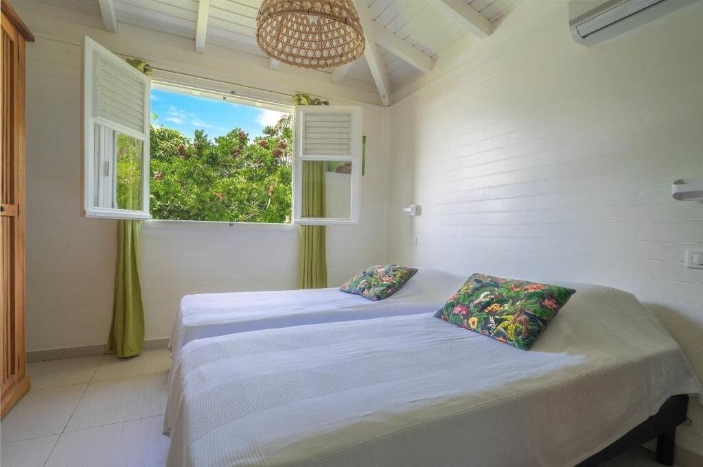 A room with two beds, a window with open shutters, and a ceiling fan.